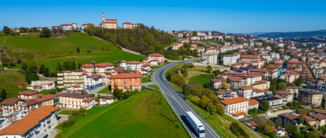 Hyperrealistic aerial drone shot of a modern moving truck driving through the picturesque Moncalieri landscape, featuring rolling hills, historic buildings, and modern residential areas under a clear sky.